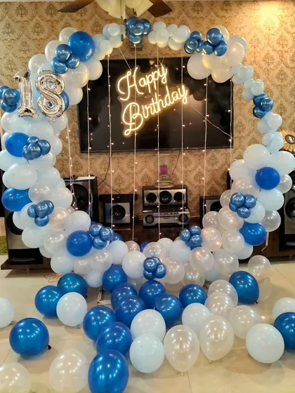 This 18th birthday ring decoration uses a blue and white color scheme. We place it in front of a TV unit, showing how we can adapt our setups to your living room space, complete with a neon sign and fairy lights.