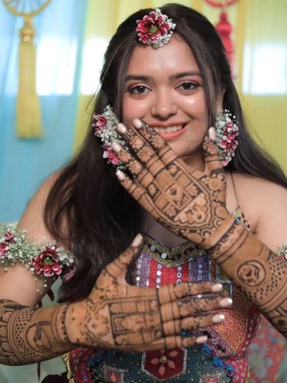 A happy bride with floral jewelry, showing off her beautiful mehandi. A perfect look for a mehandi ceremony.