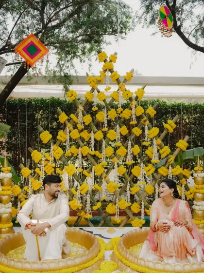 A serene moment before the Haldi madness begins. The couple sits in traditional brass urns, surrounded by a beautiful marigold decor setup.