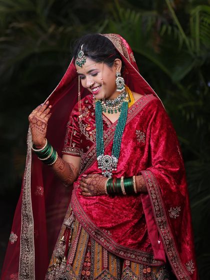 A candid moment of bridal joy. This bride looks absolutely beautiful in her red velvet lehenga, complete with stunning green bridal jewellery.