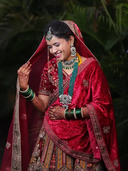 A candid moment of bridal joy. This bride looks absolutely beautiful in her red velvet lehenga, complete with stunning green bridal jewellery.