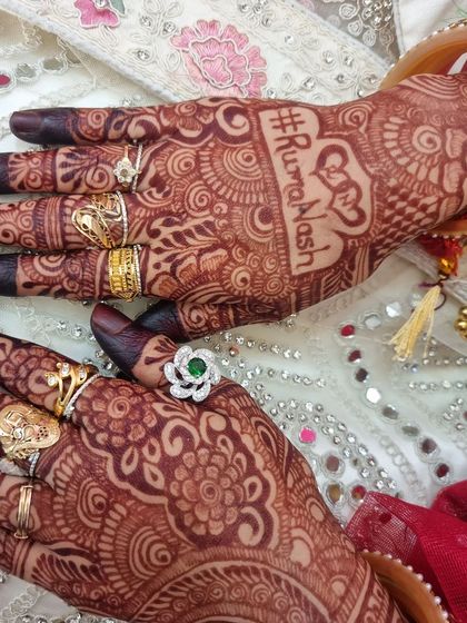 A close-up of the #RumaNash wedding hashtag, surrounded by detailed henna patterns and adorned with beautiful bridal rings.