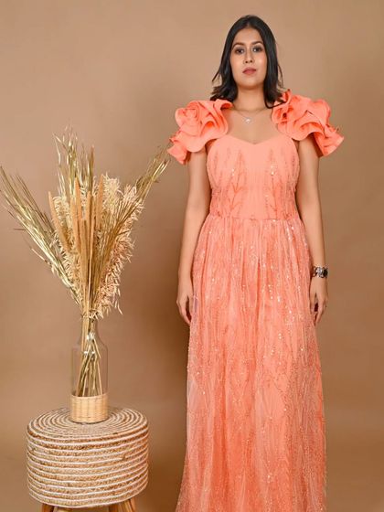 A full-length view of the coral gown with ruffled shoulders. The A-line cut is flattering for many body types and is a great option for a baby shower or daytime party.