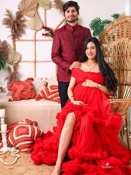 A regal portrait of the expecting couple in our boho-inspired studio. The mom-to-be is seated on a peacock chair in a vibrant red gown, creating a striking and stylish image.