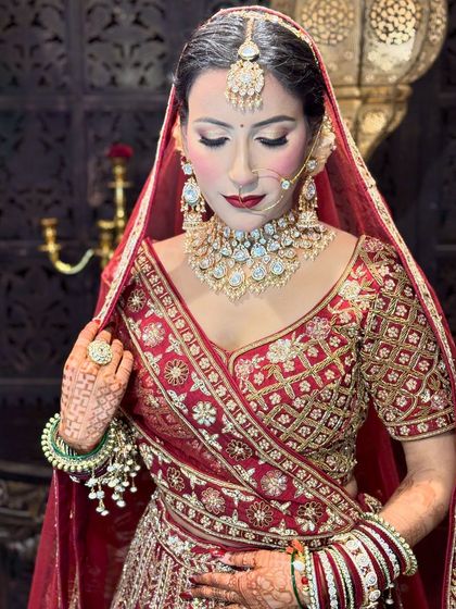 A quiet moment of reflection for the bride. Her makeup features a soft shimmer on the eyes and a classic red lip, perfectly complementing her traditional jewelry and attire.