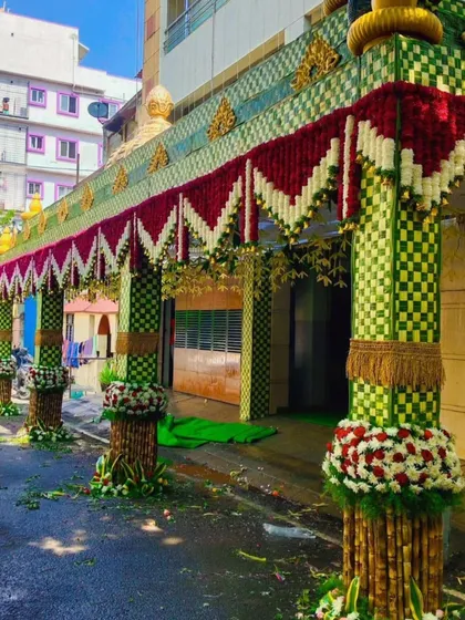 Here is a wide view of a wedding house entrance. I created a large *chappara* with checkered-pattern woven leaves and pillars decorated with sugarcane and fresh flowers.