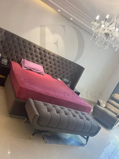 A grand bedroom featuring a bed with an extra-tall, tufted headboard in dark grey. Paired with a matching bench and a crystal chandelier, this room is the definition of opulent comfort.