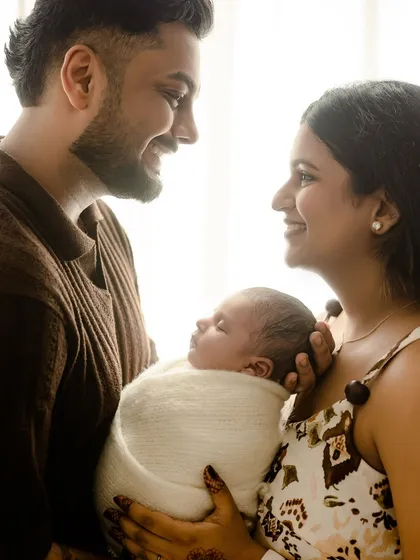 New parents gazing at each other with smiles while holding their sleeping baby. This photo captures the love that created their new family.
