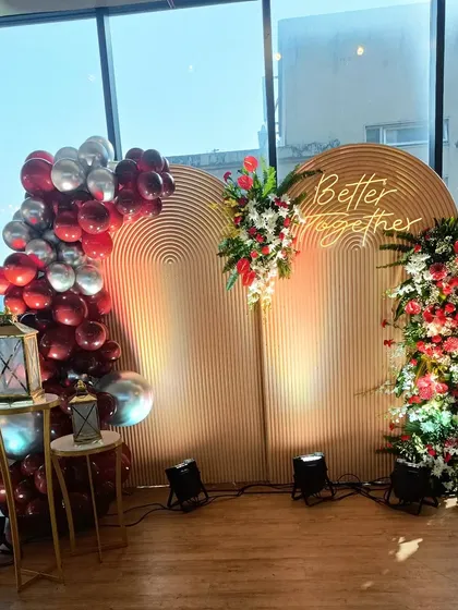 To celebrate an anniversary, I designed this 'Better Together' backdrop. It combines modern ribbed wooden panels with lush red and white floral arrangements and a cascade of red and silver chrome balloons, creating a romantic and sophisticated look.