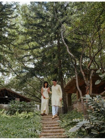 A candid moment of the couple walking down a rustic path at The Tamarind Tree in Bangalore. Their light, coordinated outfits and the lush greenery create a fresh and natural pre-wedding portrait.