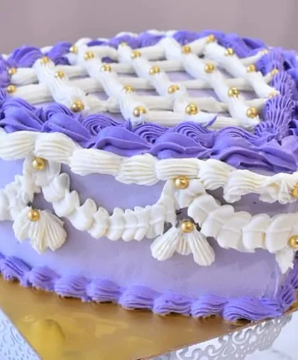 A trendy vintage-style heart cake in a lovely lavender hue. This cake showcases intricate piping techniques, including lattice work, shells, and swags, all accented with gold pearls.