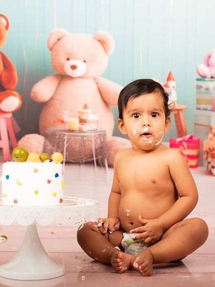 A classic 'uh oh' moment during a cake smash. The frosting on the face and the wide-eyed look make for an adorable and funny photograph.