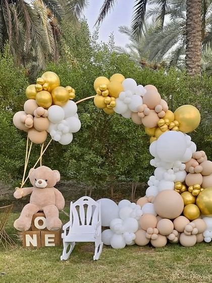A wider view of the charming teddy bear themed first birthday party, showcasing the full balloon arch and the light-up number '1' in a garden setting.