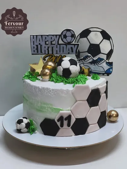 A football theme cake for an 11th birthday. This cake features a hexagonal pattern, a 3D football, and shoe toppers, all on a whipped cream frosted base.