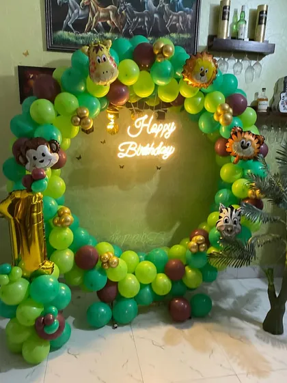 A fun jungle-themed birthday party with a full ring of green balloons. We decorated the ring with various animal head foil balloons and a 'Happy Birthday' neon sign for a lively safari vibe.