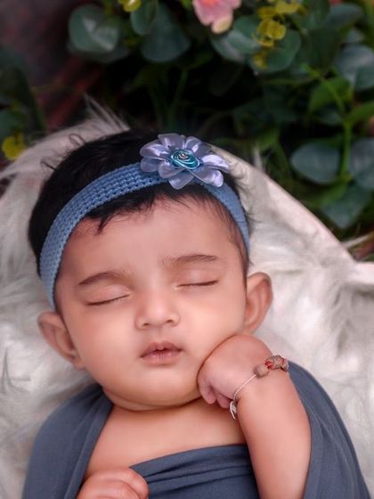 A lovely close-up of a sleeping baby girl, showing off her beautiful hair and a simple blue floral headband.