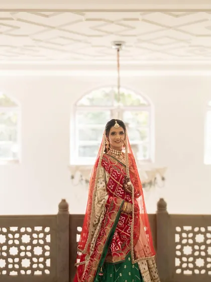 This full-length portrait captures the grandeur of a traditional Gujarati bride. The makeup is designed to be flawless from afar, ensuring the bride looks majestic and feels confident throughout her special day.