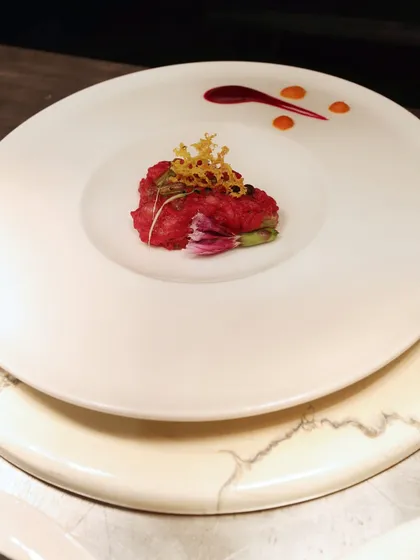 A vibrant red dish, possibly a beetroot risotto or tartare, crowned with a delicate, crispy garnish. The colour is bold, and the plating is precise.