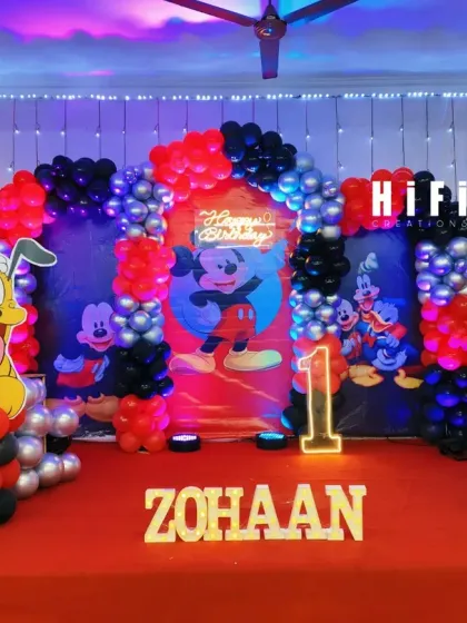 A classic Mickey Mouse Clubhouse birthday party theme. This stage setup features a red, black, and silver balloon arch, character cutouts of Mickey and Pluto, and a personalized backdrop.