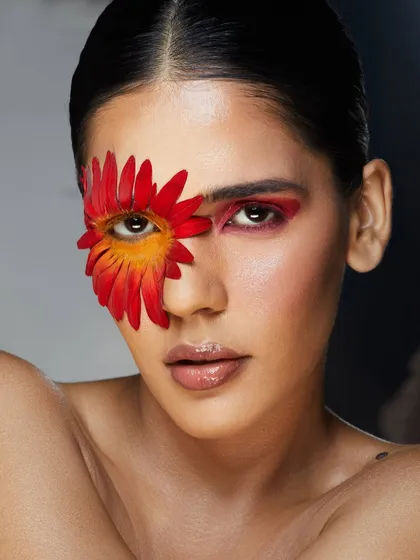 A creative floral look where a red and yellow flower is used as an artistic patch over one eye.