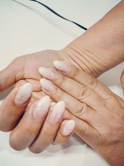 A simple and clean look with a soft, shimmery white glitter polish on natural, almond-shaped nails.