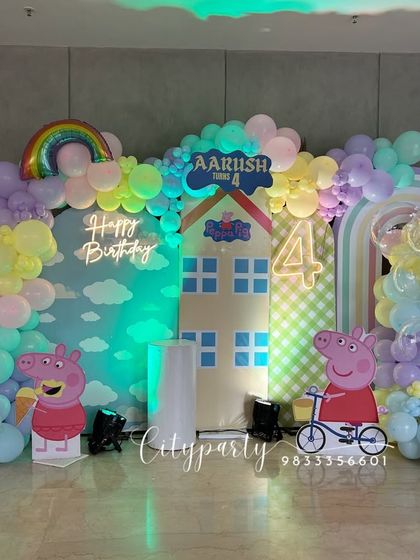 A playful Peppa Pig theme for a 4th birthday celebration. This large-scale setup features multiple backdrops creating a Peppa Pig world, character standees, a rainbow balloon, and a 'Happy Birthday' neon sign.