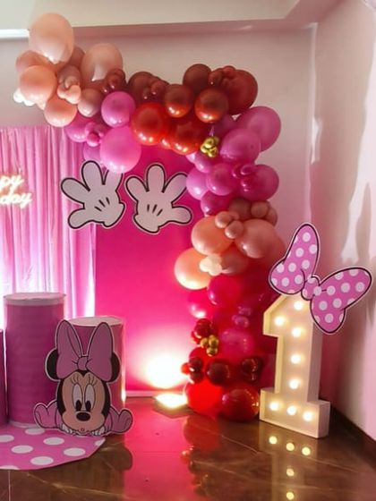 This angle highlights the light-up marquee number '1' and the Minnie Mouse cutouts. The balloon arch uses a mix of chrome and pastel balloons to add depth and texture to the overall first birthday design.