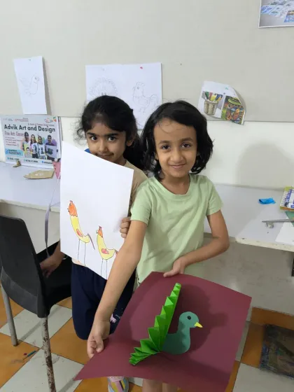 Our youngest students exploring different art forms. One student shows her bird drawing while another displays her 3D paper-craft bird.