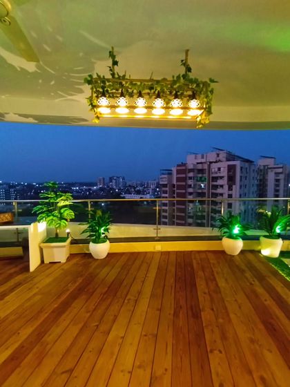Looking out from the wooden deck of the Rajkot balcony. The city view at dusk combined with the warm lighting and greenery creates a perfect urban oasis.