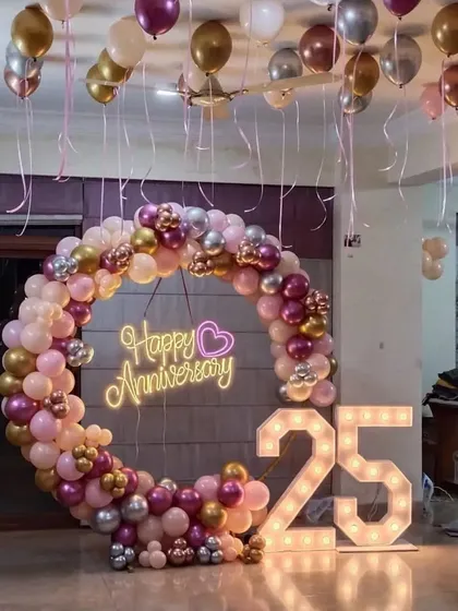 A similar 25th-anniversary setup with a circular balloon arch in pink, gold, and silver, along with marquee numbers.
