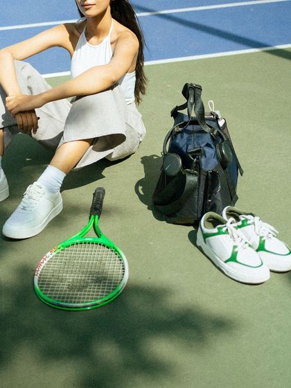 A detailed shot focusing on the accessories. By cropping the model, the image draws attention to the tennis racket, shoes, and the Lino Perros bag, making them the heroes of the shot.