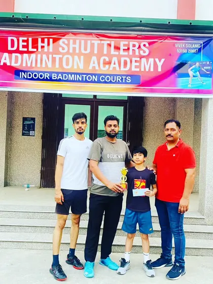 A young champion with his trophy, standing with our coaches in front of the Delhi Shuttlers Badminton Academy banner. We provide end-to-end support for our competitive players.