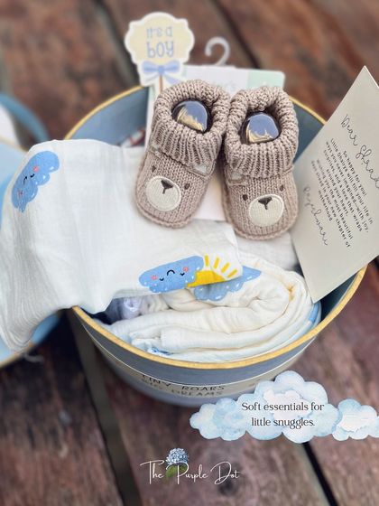 Soft essentials for little snuggles. This powder-blue hat box is filled with cozy bear-themed booties, a printed swaddle, and a personalized welcome card for a new baby boy.