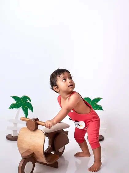 A playful shot of a baby standing with a wooden scooter prop in the studio, perfect for capturing their developing mobility and curiosity.