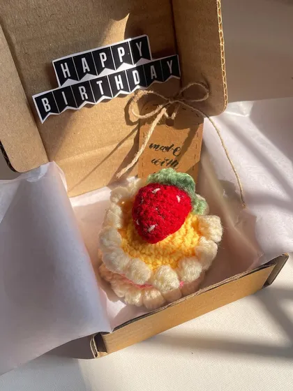 The crochet cake, packed and ready to be gifted for a birthday. The "Happy Birthday" banner adds a festive touch.