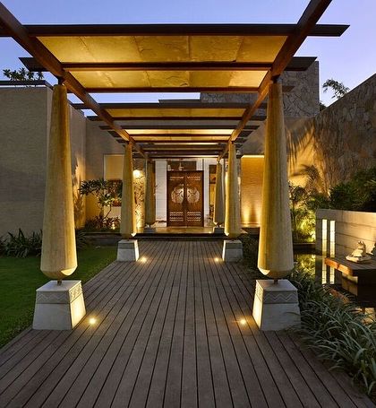 The entrance to C Farm in Chattarpur features a wooden deck walkway flanked by sculptural columns, leading to a grand door. The design uses a covered pergola to create a dramatic sense of arrival and transition from the outside world.