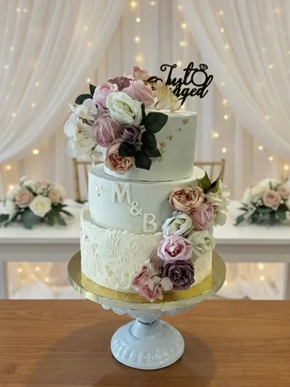 For engagements and weddings, I design elegant tiered cakes like this one. It features a soft, textured buttercream finish, delicate gold leaf accents, and a beautiful arrangement of fresh flowers, all customized with the couple's initials for a personal touch.