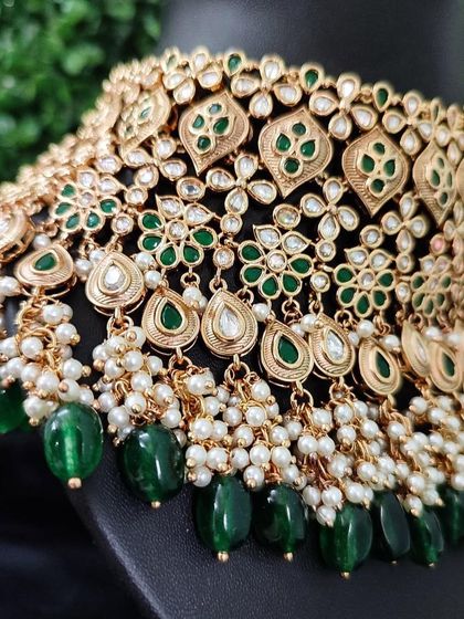 A close-up of a green kundan necklace with delicate pearl and bead drops.
