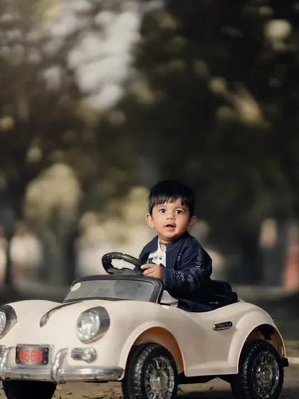 A cool little driver ready for the open road. The vintage car and wooded path give this photo a timeless, adventurous feel.