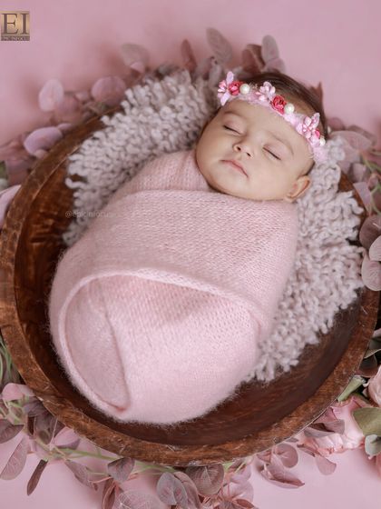 The full floral bowl setup, showing the baby snugly wrapped and surrounded by a wreath of beautiful pink flowers and greenery.