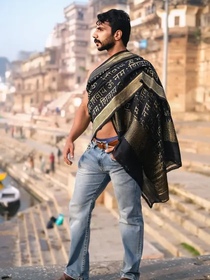 A modern take on tradition, this portrait captures a powerful stance against the backdrop of the ancient ghats, with the sacred text on the drape adding a spiritual layer.