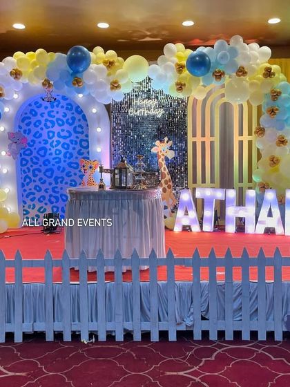 Another take on the jungle theme for Atharva's first birthday. This setup includes a white picket fence, cute cartoon animal cutouts, and a blue leopard-print arch.