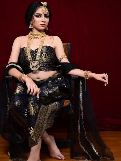 A powerful pose in the black and gold dhoti-saree, showcasing the intricate gold patterns and the off-shoulder blouse. This outfit is paired with our traditional gold temple jewellery.