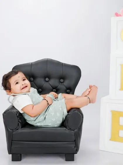 A playful and relaxed shot from the classic white session. Posing the baby in this tiny black armchair adds a touch of modern style and captures a candid, happy moment during the celebration.