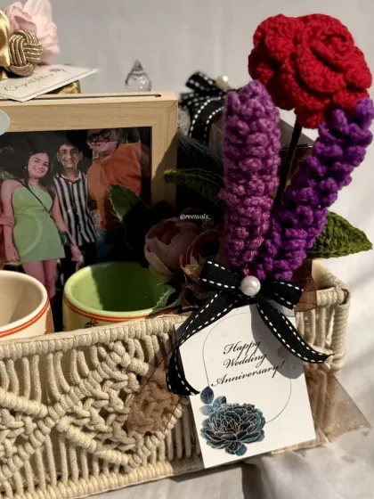 A cozy anniversary hamper in a macrame basket. It includes a personalized photo frame, crochet flowers, and a 'Happy Wedding Anniversary' tag, making it a heartfelt gift.