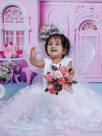 A joyful wave from our little fairy. The pink dollhouse backdrop adds to the enchanting, fairytale atmosphere.