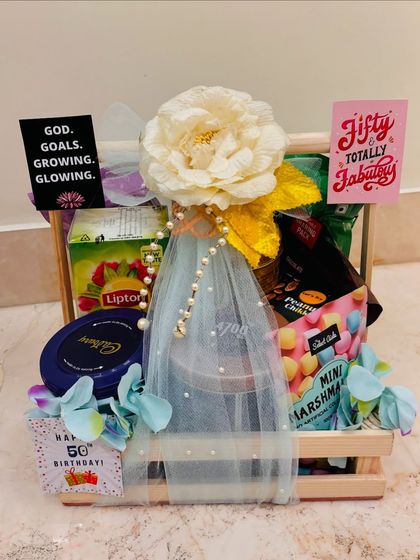 A delightful hamper for a golden 50th birthday milestone. This crate is filled with treats like Lipton tea, Cadbury chocolate, and mini marshmallows, all beautifully wrapped.