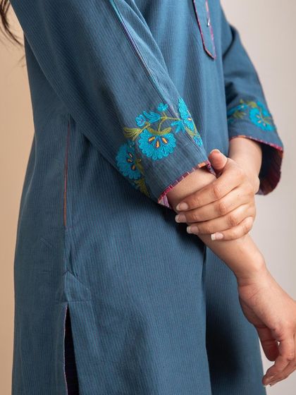 A close-up of the sleeve of our Haveli Crewel Blue Kurta. The rich blue-green hue of the cotton fabric is beautifully complemented by the vibrant floral embroidery.