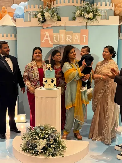 A heartwarming cake-cutting moment with the family in front of the castle backdrop. The custom Mickey-themed cake sits on a pedestal, ready for the celebration.