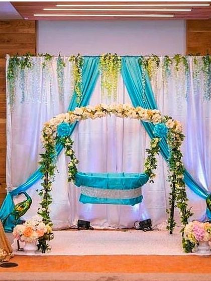 A beautiful peacock-themed cradle decoration. The setup uses turquoise drapes and a floral arch, with peacock figures on either side, symbolizing grace and beauty.